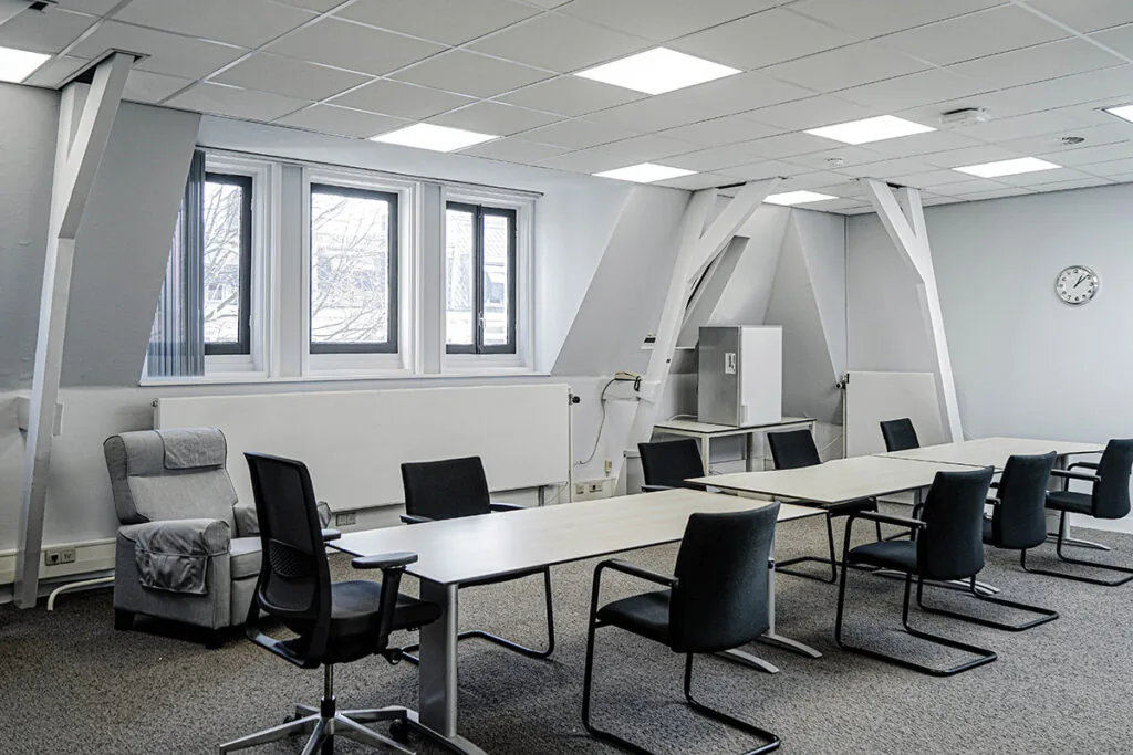 Vergaderruimte aan de Burgemeester van Karnebeeklaan met moderne inrichting, witte tafels en zwarte stoelen.